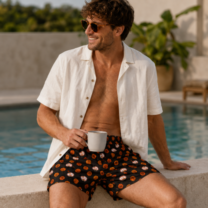 Man in white shirt and Weunderlust boxer shorts sitting by a pool holding a cup.